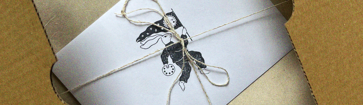 A square kraft paper gift box with a white inner card tied with twine and a black printed illustration of a hare, photographed close-up against a brown cardboard background.